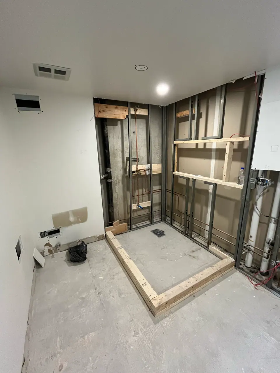 The shower opening framed out in steel stud with timber blocking let into the wall for a future bench and niche. The curb is built up in dimensional lumber and the drain body is already set.