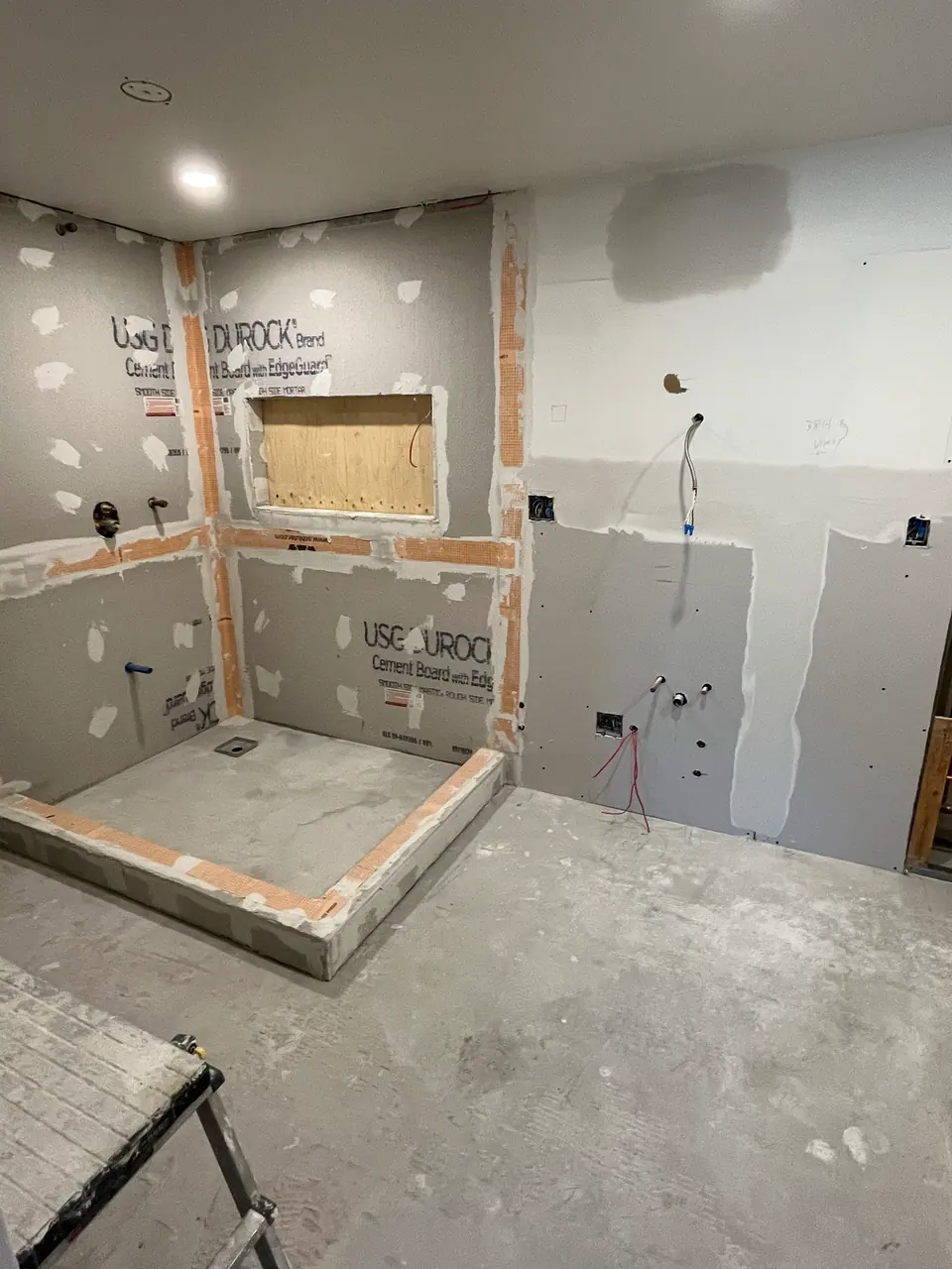 The shower enclosure sheathed in cement board with waterproofing membrane banded across every seam and inside corner in orange. The recessed niche is blocked in plywood and the sloped curb is wrapped and sealed.
