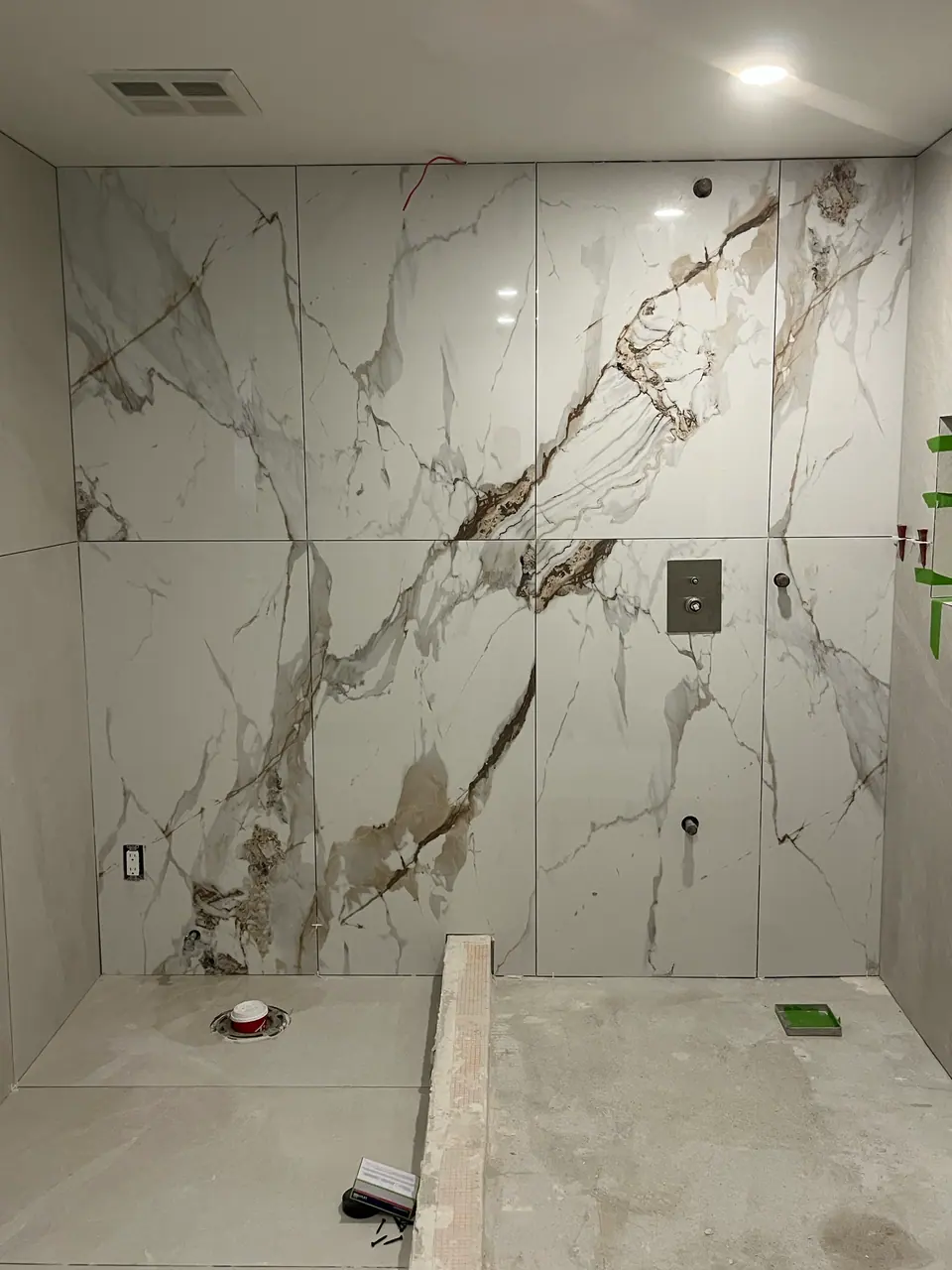 The feature wall square on: four porcelain panels book-matched so the veining opens symmetrically across the joint like a mirrored pair. Leveling clips are still in place along every seam.