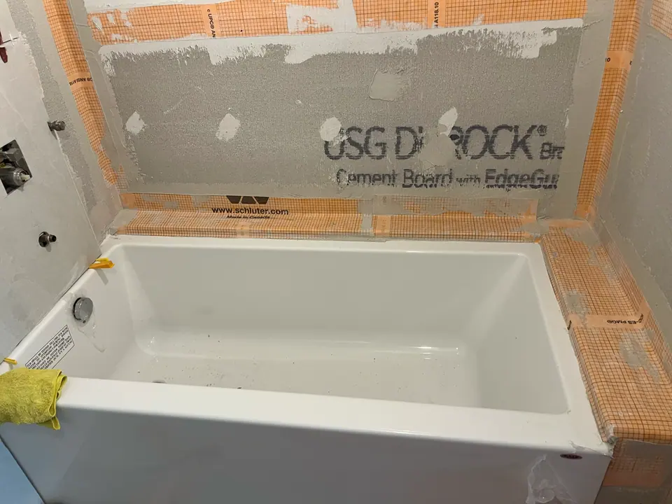 A new alcove tub set and levelled, with cement board above it and waterproofing membrane banded along the tub flange and up both inside corners before any tile goes on.